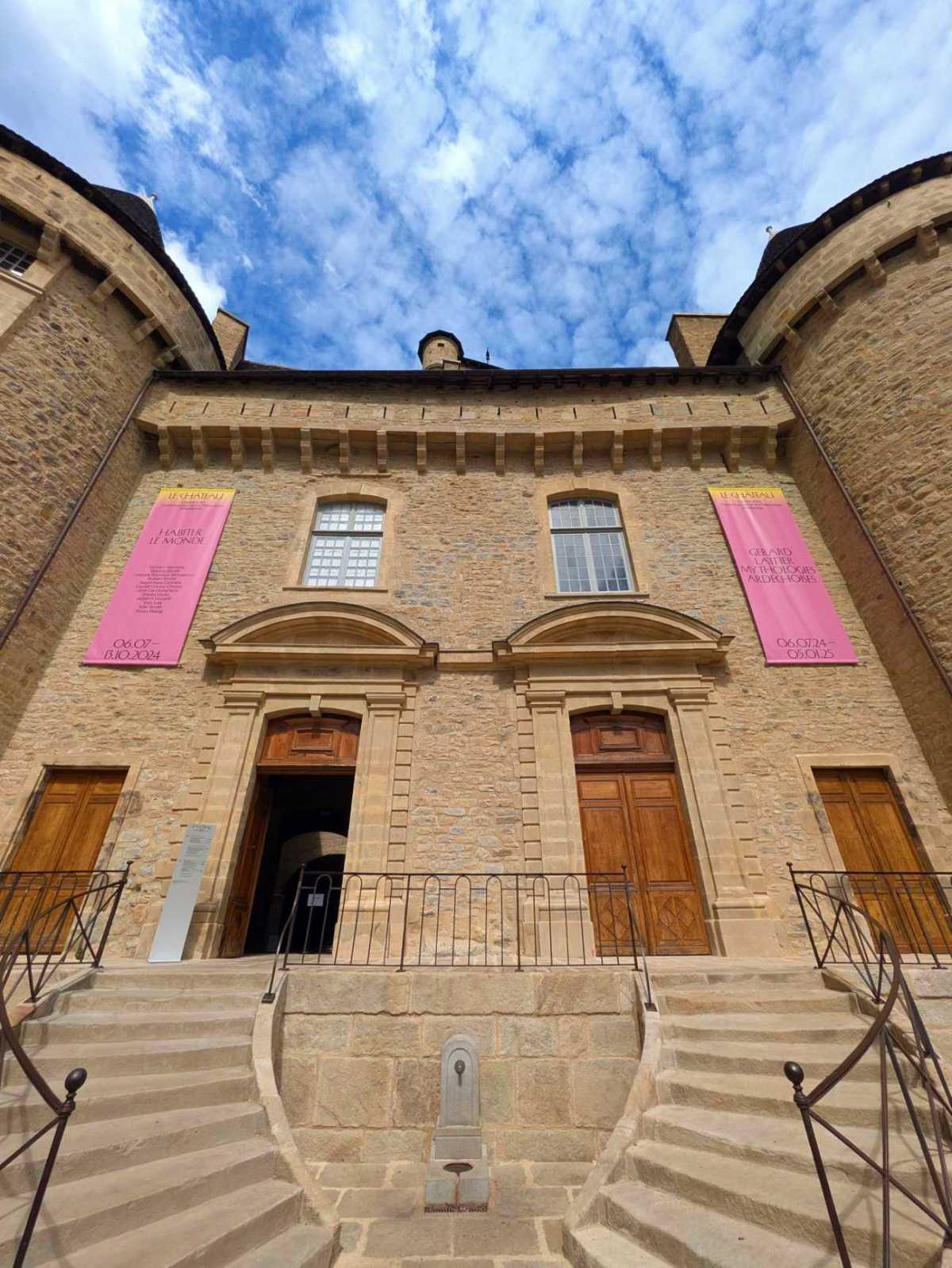 Vue sur l'entrée du château d'Aubenas, avec les panneaux de l'exposition "Habiter le monde"