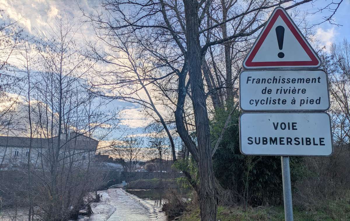 Voie vélo submersible qui traverse le Luol, affluent de l'Ardèche, avec un panneau de signalisation